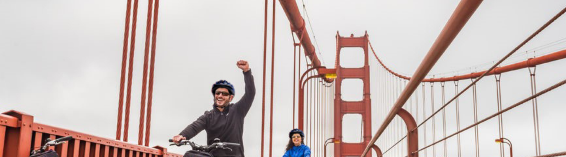 A man holds up his arm in victory as he and another rider bike across the Golden Gate Bridge