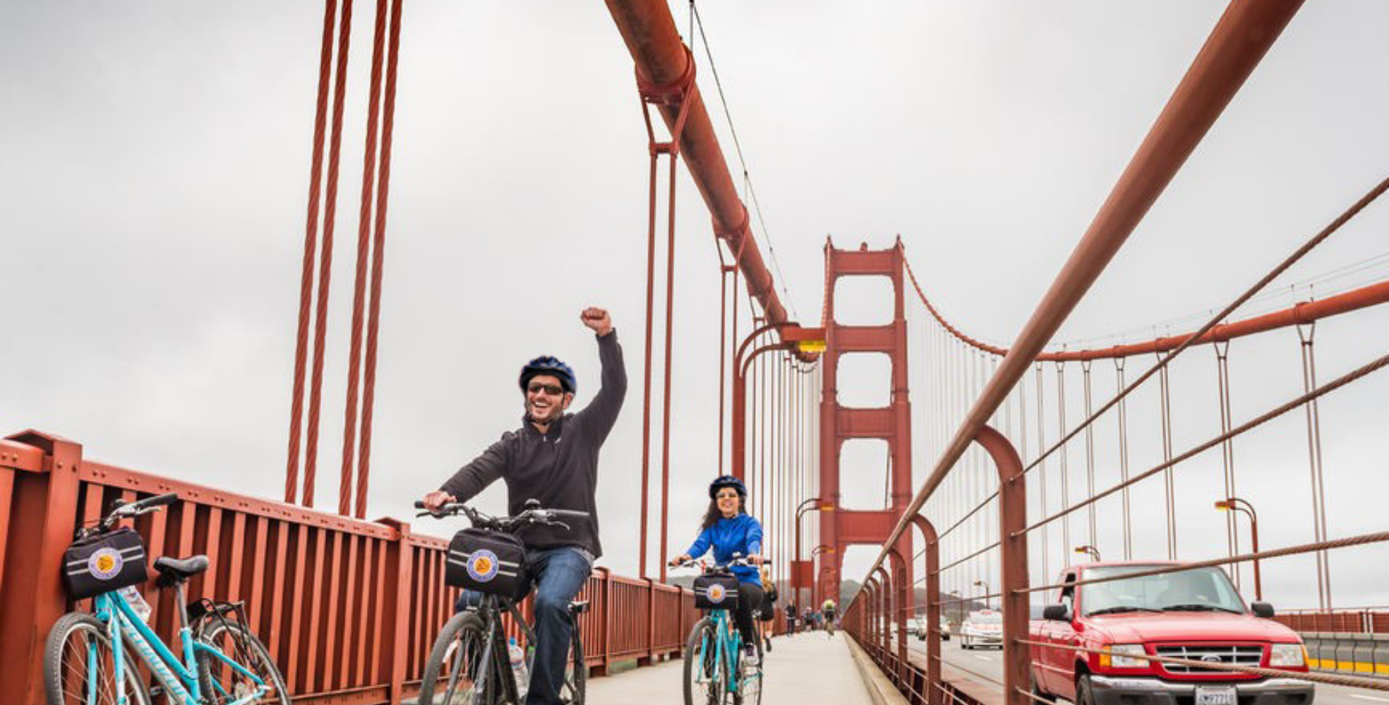 A man holds up his arm in victory as he and another rider finish riding bikes across the Golden Gate Bridge