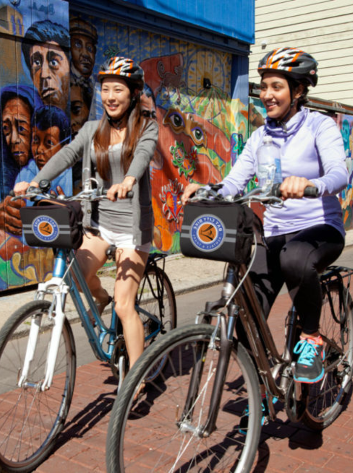 two women riding bikes in a neighborhood in san francisco with a mural in the background