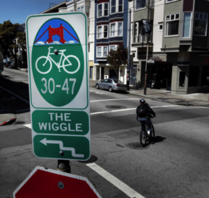 a sign reading 'the wiggle' with a person riding a bike behind it