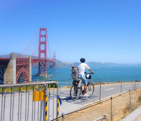 a dad and his baby biking on a path by the golden gate bridge