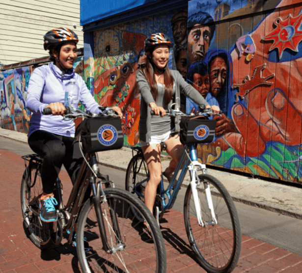 two women riding bikes in mission district, one of the best sf neighborhoods for food