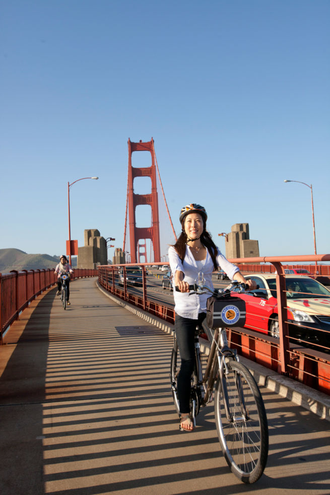 a woman rides a rented bicycle across the golden gate bridge